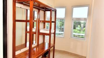 Una habitación con un armario de madera, dos ventanas con vistas a zonas verdes y suelo de baldosas.