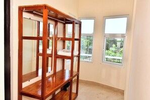 A room with a wooden wardrobe, two windows with a view of greenery, and a tiled floor. - Grami Cafe (Puducherry)
