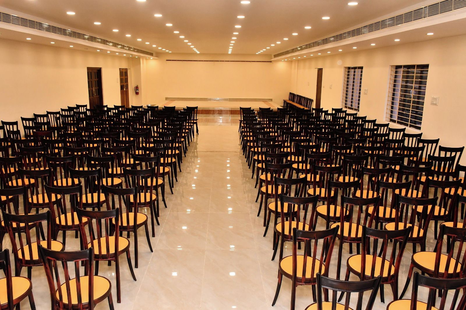 Un salón de conferencias con filas de sillas orientadas hacia un escenario, con luces en el techo y un extintor.
