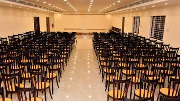 Un salón de conferencias con filas de sillas orientadas hacia un escenario, con luces en el techo y un extintor.