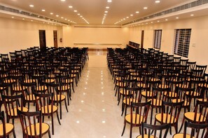 A conference room with rows of chairs facing a stage, equipped with ceiling lights and a fire extinguisher.