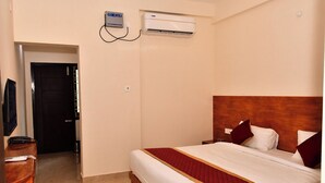 A hotel room with a bed, a television, a desk, and an air conditioning unit. - Grami Cafe (Edayarpalayam)