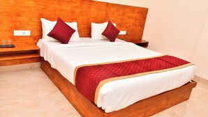 A neatly made bed with a wooden headboard, white bedding, and red accents. - Grami Cafe (Edayarpalayam)