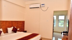 A hotel room with a bed, bedside table, air conditioning unit, and a view of the outdoors. - Grami Cafe (Edayarpalayam)