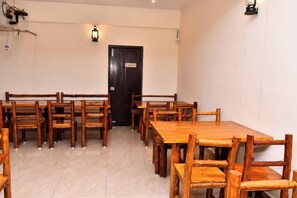 A room with a large wooden table and chairs, a door with an emergency exit sign, and a light fixture on the wall.