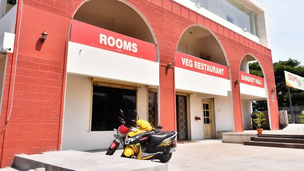 A building with a red and white facade, featuring signs for 'ROOMS' and 'VEG RESTAURANT' with an arched entrance. - Grami Cafe (Edayarpalayam)