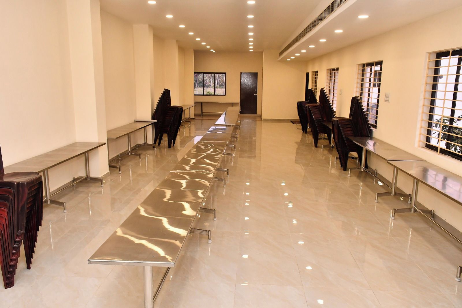 Una sala larga y estrecha con suelo reflectante, filas de sillas y mesas a lo largo de las paredes.