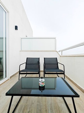 A balcony with a glass table, two chairs, and a decorative canister.