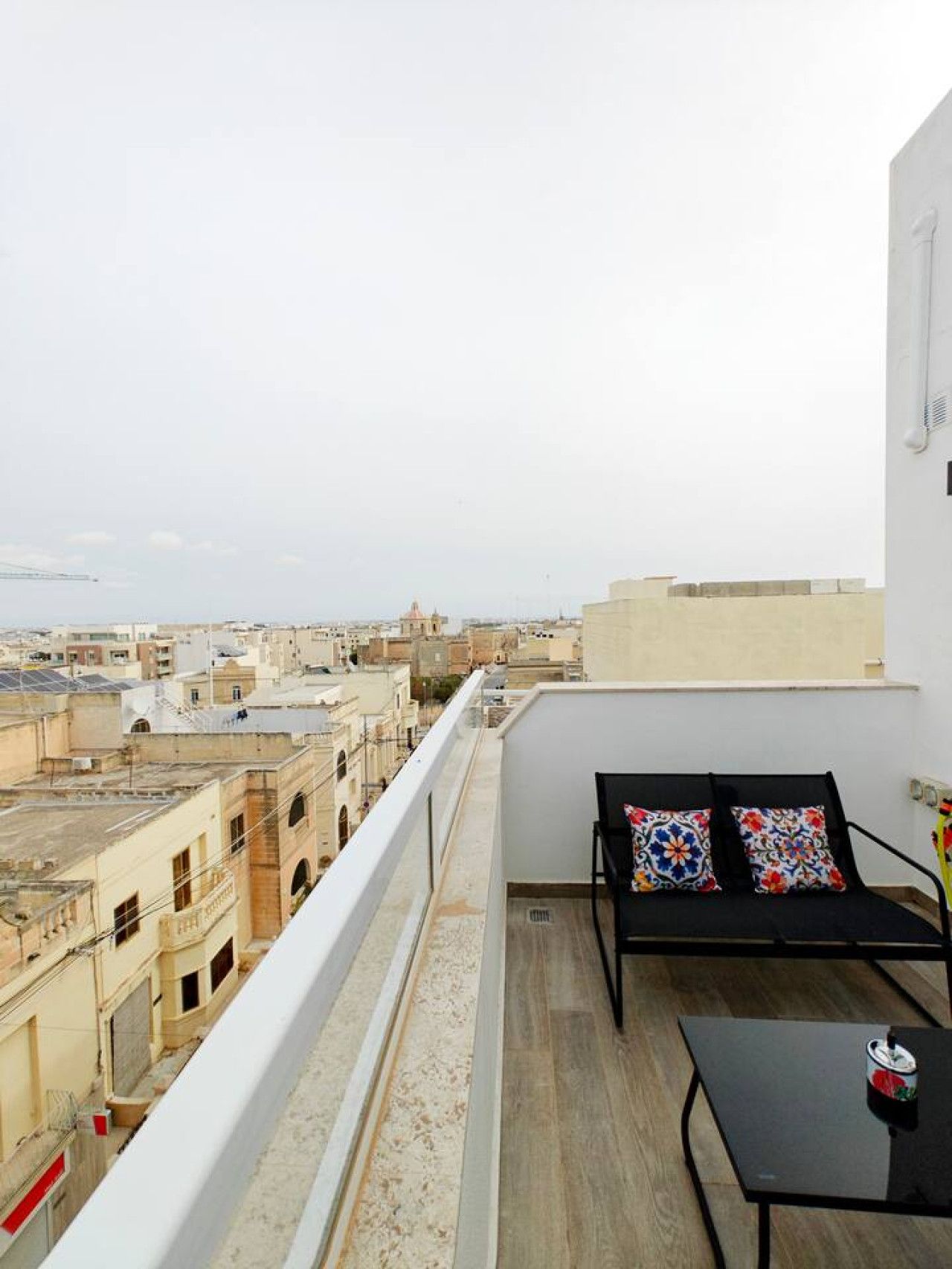Varanda com sofá e mesa, com vista para a paisagem urbana.