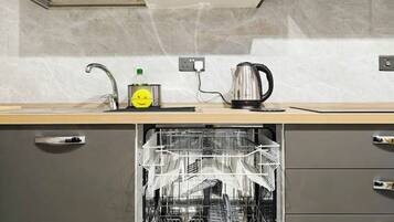 Una cucina moderna con mobili grigi, una lavastoviglie in acciaio inossidabile e un piano di lavoro con un bollitore e una bottiglia.