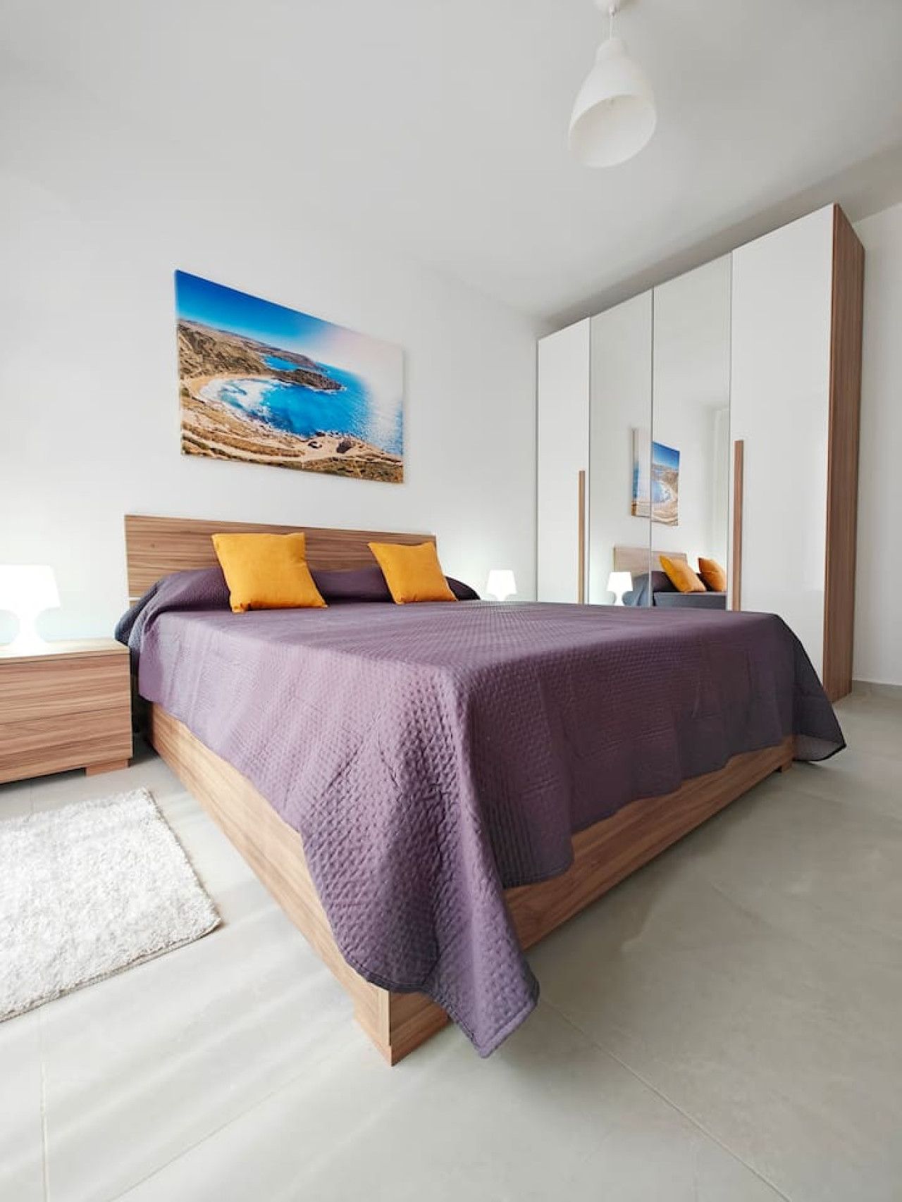 Een moderne slaapkamer met een groot bed, een nachtkastje, een bedtafel en een wandlamp.