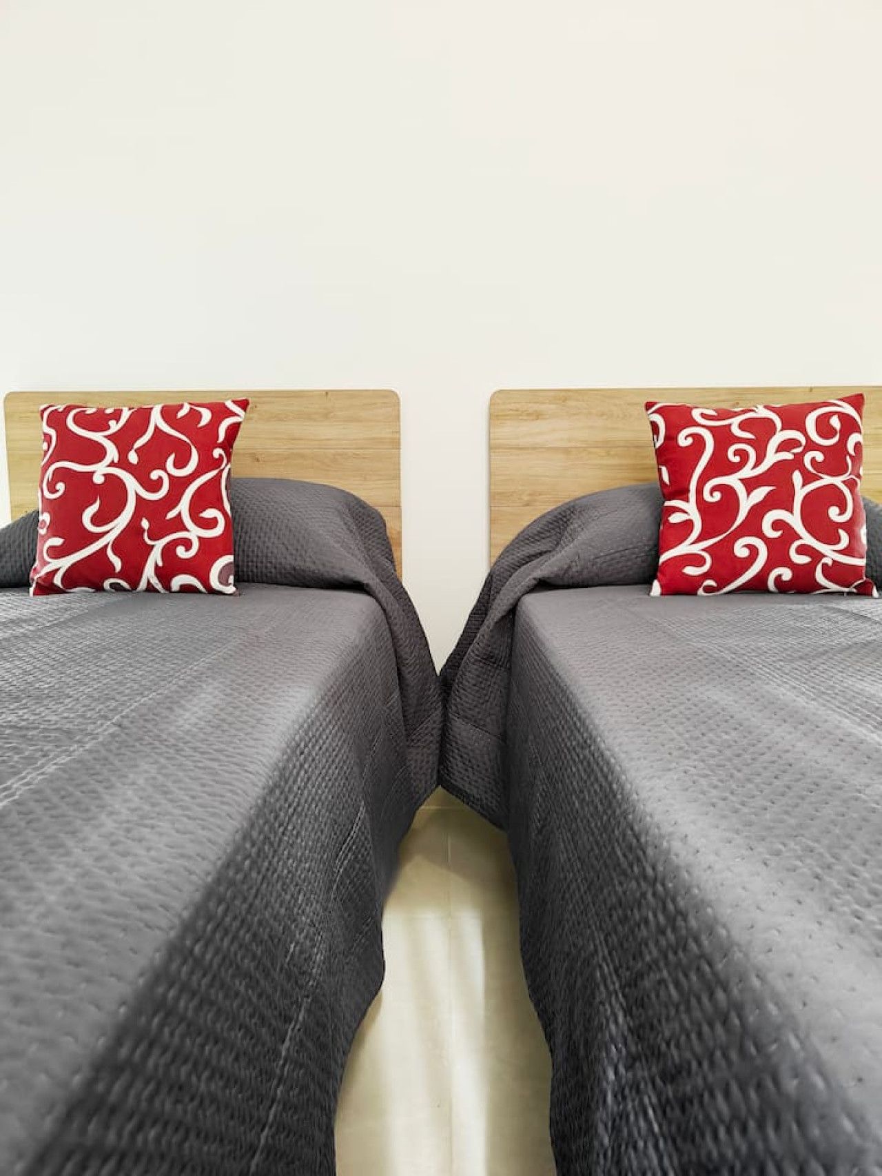 Une chambre avec deux lits, chacun doté d’une tête de lit en bois et d’un oreiller à motifs rouges.