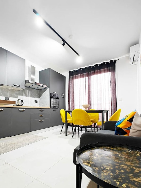 A modern kitchen with grey cabinets, a black countertop, and a dining area with yellow chairs.