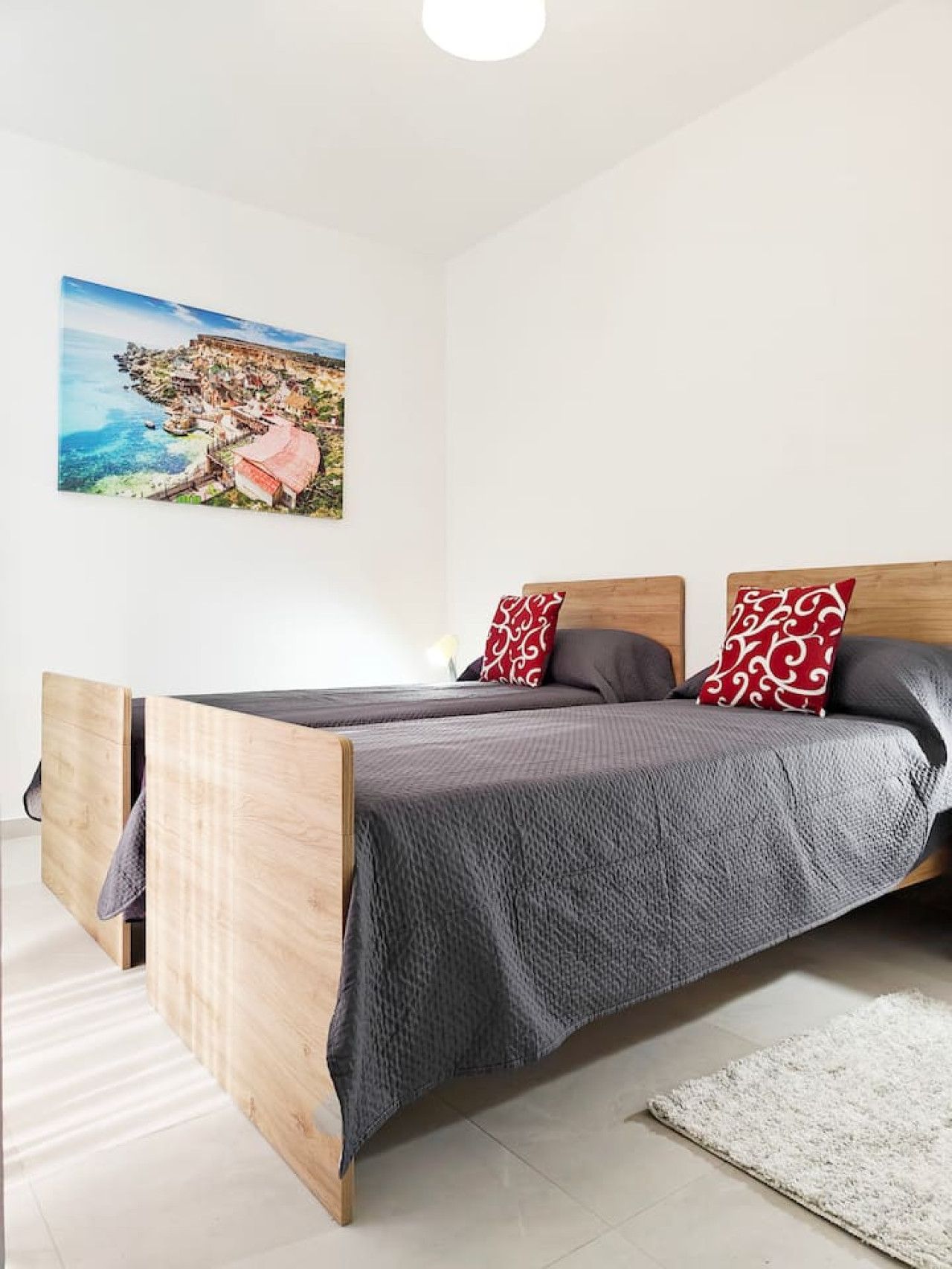 A bedroom with a wooden bed, a gray blanket, and red patterned pillows.