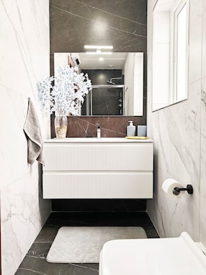 A bathroom with a white vanity, a mirror, a towel rack, a flower vase, and a toilet. - White tulip apartment (Safi)