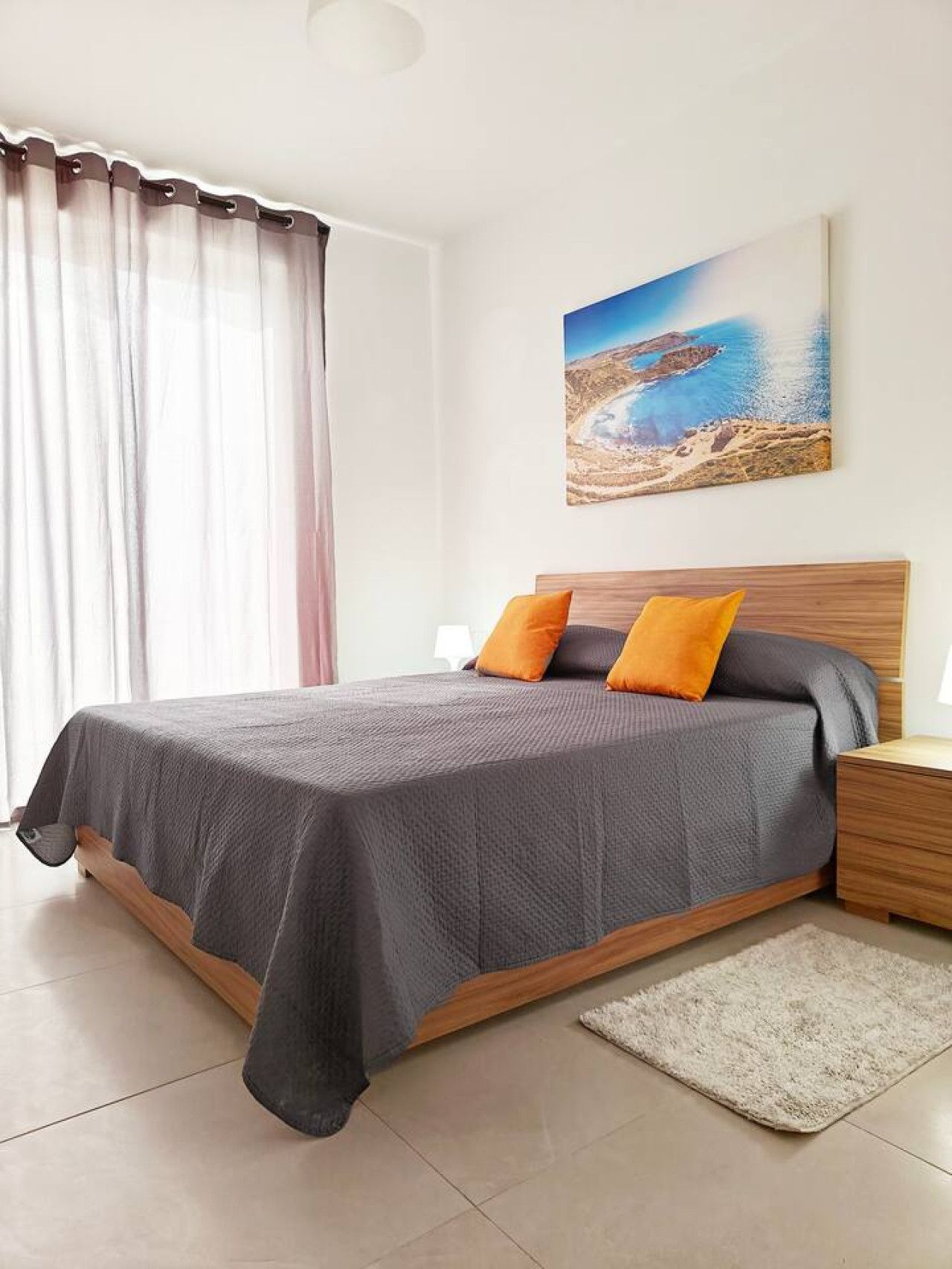 Una camera da letto con un letto, cuscini, un comodino, un tappeto e un quadro appeso al muro.