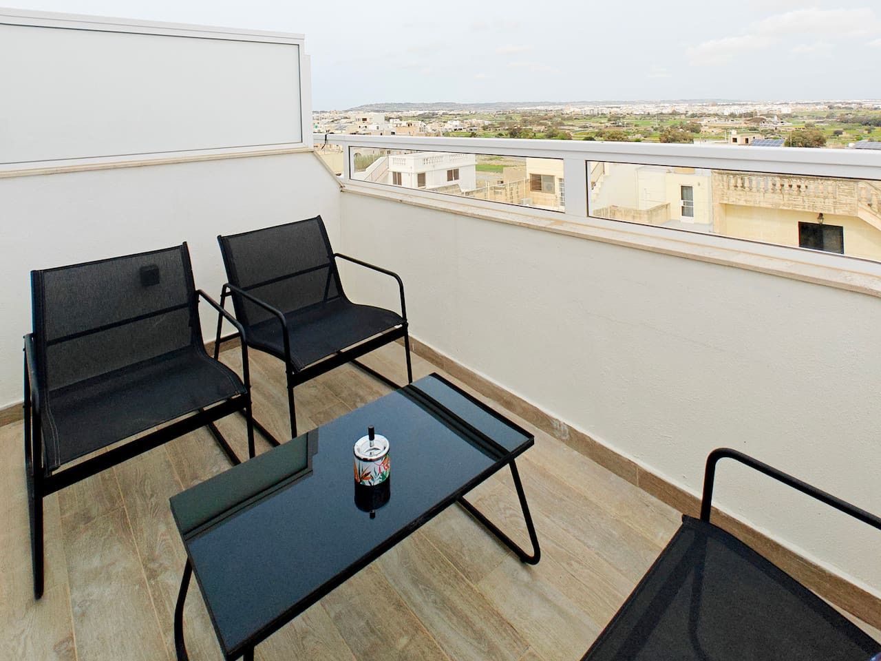 Un balcon avec deux chaises et une petite table, une canette de boisson et une vue sur les immeubles.