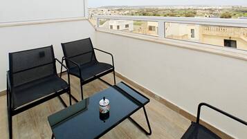 Un balcon avec deux chaises et une petite table, une canette de boisson et une vue sur les immeubles.