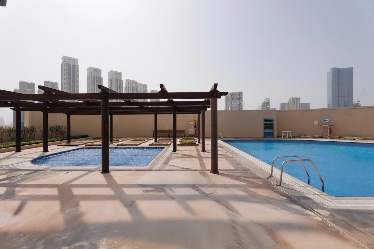 A rooftop swimming pool with a pergola, a separate hot tub, and a view of the city skyline.