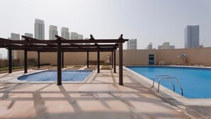 Piscina no terraço com pergolado, uma banheira de hidromassagem separada e vista para o horizonte da cidade.