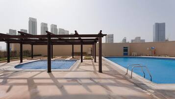 A rooftop swimming pool with a pergola, a separate hot tub, and a view of the city skyline.