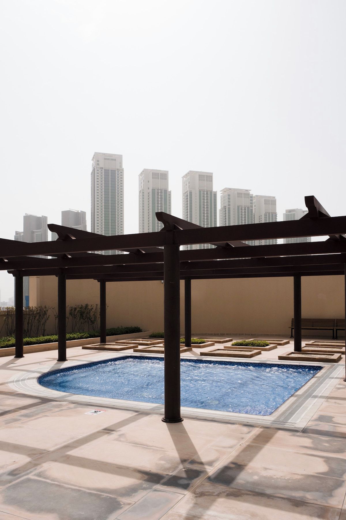 Área de piscina no terraço com estrutura de pérgola, cercada por um horizonte urbano de arranha-céus.
