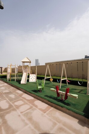 An outdoor play area with a slide, swings, and a climbing structure.