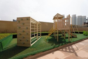 A playground with climbing structures and a slide, set on artificial turf with a cityscape in the background. - Vanilla Homes Modern 1BR in Reem Island (Abu Dhabi)