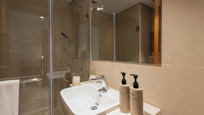 Casa de banho moderna com chuveiro em cabine de vidro, lavatório branco e dois frascos de produtos de higiene.