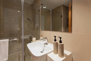 A modern bathroom with a glass-enclosed shower, a white sink, and two toiletry bottles. - Vanilla Homes Modern 1BR in Reem Island (Abu Dhabi)
