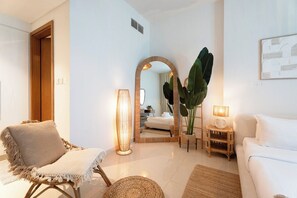 A modern living room with a white sofa, a wicker chair, a large mirror, and a floor lamp.