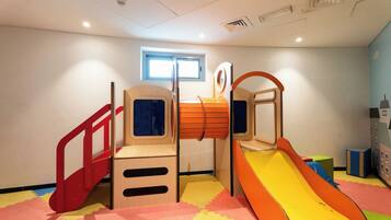 Un espace de jeux pour enfants avec un toboggan, des structures d’escalade et une fenêtre.