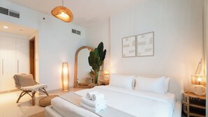 Quarto de hotel com uma cama grande, uma cadeira, uma mesa de cabeceira com abajur e um espelho.