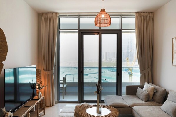 A modern living room with a large flat-screen TV, a sofa, a coffee table, and a view of a cityscape through large windows.