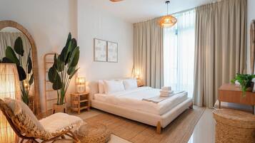 Quarto moderno com uma cama grande, mesas de cabeceira, uma cadeira e um espelho amplo.