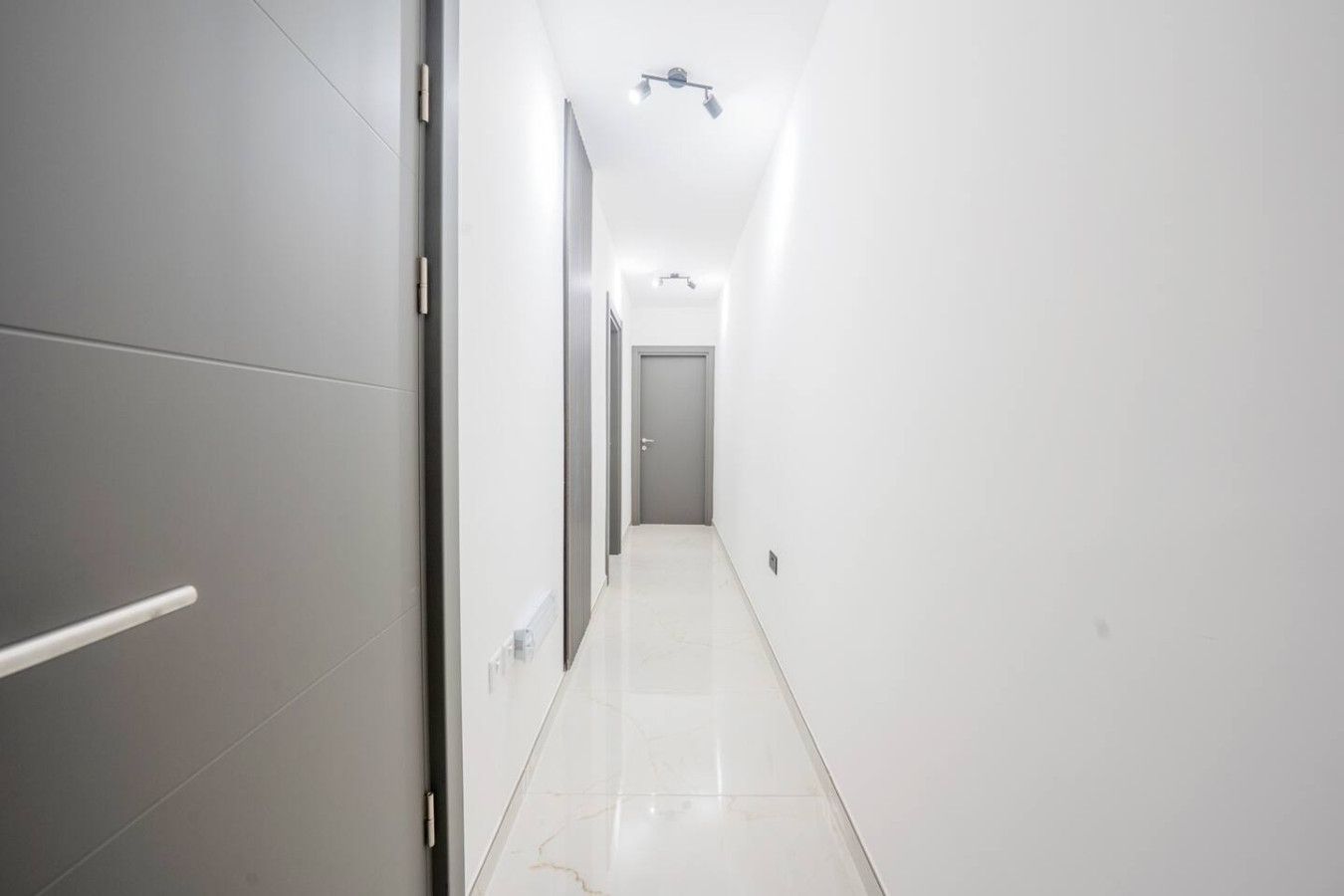 A narrow, well-lit hallway with a door at the end, leading to a room.