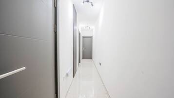 A narrow, well-lit hallway with a door at the end, leading to a room.