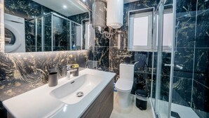 Un baño moderno con salpicadero de mármol, un lavamanos grande, inodoro y cabina de ducha con paredes de vidrio.