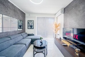 Ein modernes Wohnzimmer mit einem grauen Ecksofa, einem runden Couchtisch und einem Flachbildfernseher.
