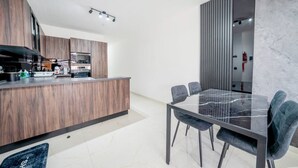 Una cocina moderna con armarios de madera, encimera de mármol y comedor con mesa y sillas de vidrio.