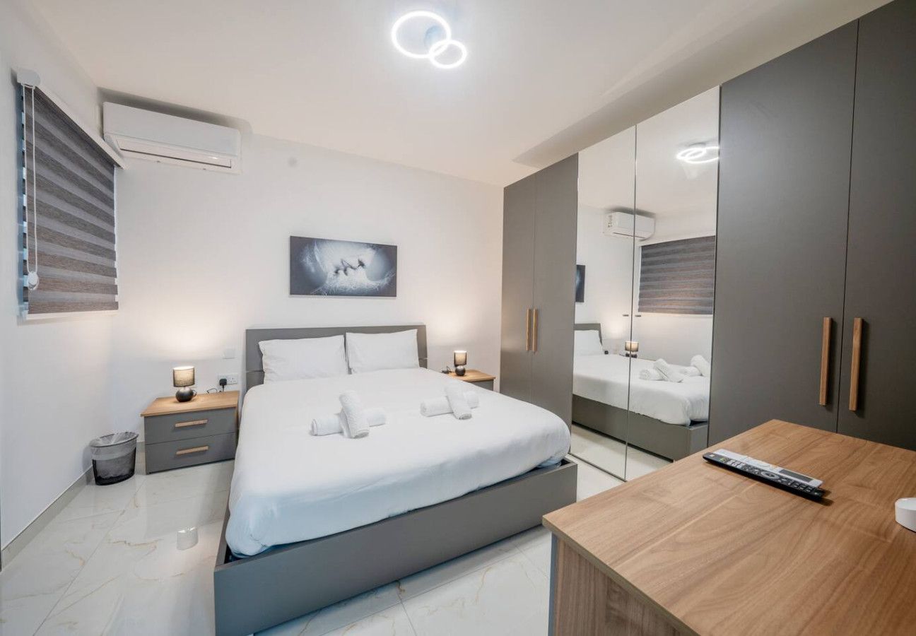 A modern bedroom with a bed, bedside tables, a mirror, and a wooden desk.