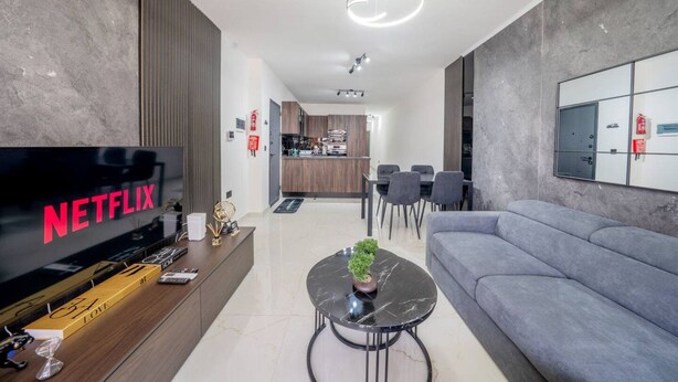 Una sala moderna con una televisión de pantalla plana, un sofá, una mesa de centro y una cocina al fondo.