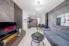 Una sala moderna con una televisión de pantalla plana, un sofá, una mesa de centro y una cocina al fondo.