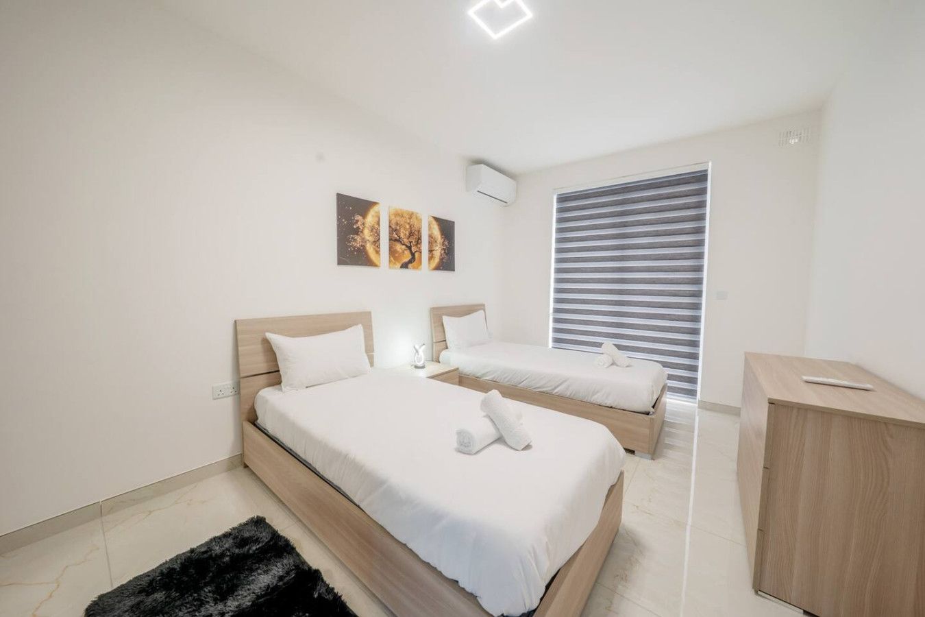 Une chambre moderne avec deux lits, un tapis noir, une table de chevet et une fenêtre avec des stores.