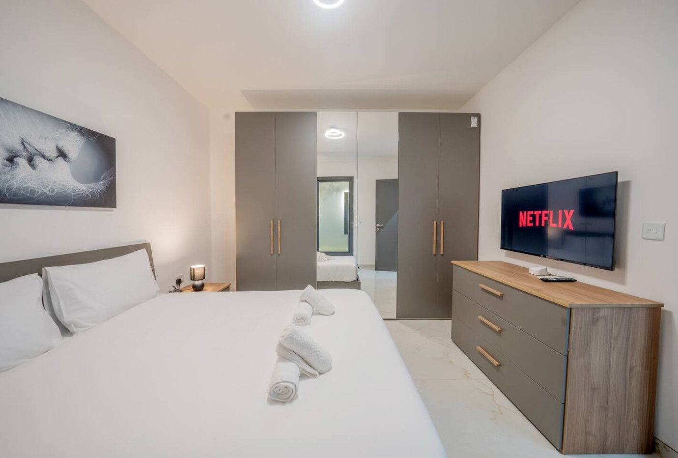 A modern hotel room with a large bed, a TV, a wardrobe, and a painting on the wall.