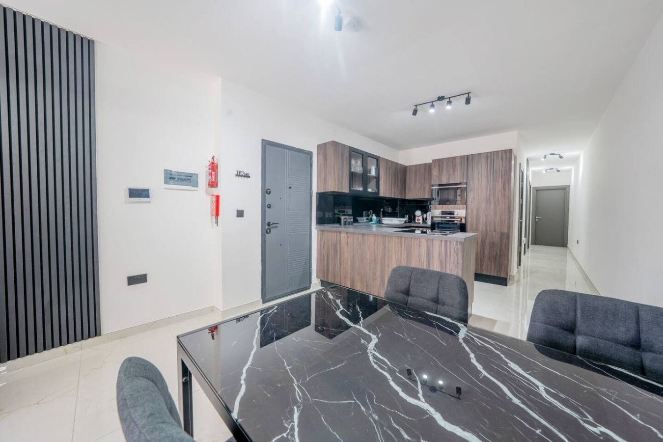 A modern kitchen with wooden cabinets, a central island, and a dining area with a glass table and chairs.