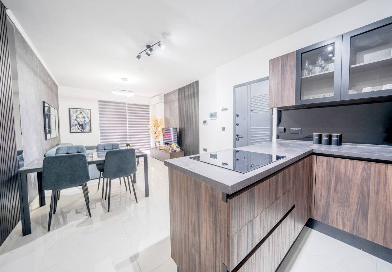 A modern kitchen with a central island, built-in cabinets, and a dining area with chairs.