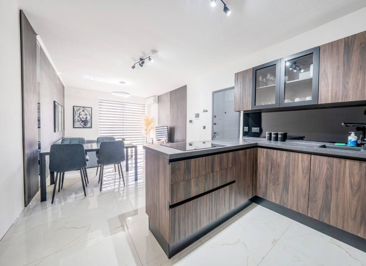 A modern kitchen with a central island, built-in cabinets, and a dining area with chairs.