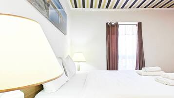 A hotel room with a bed, a lamp, a window with curtains, and a painting on the wall.