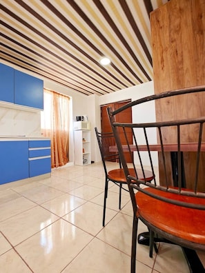 A dining area with a wooden table and chairs, a blue kitchen area with cabinets, and a striped ceiling. - The Boat House apartment (Wied il-Għajn)